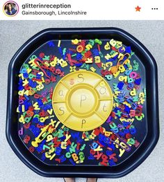 someone is holding a tray with letters and numbers on it that has a golden disc in the middle