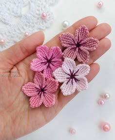 three crocheted flowers are in the palm of someone's hand, with pearls around them