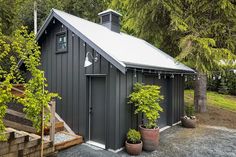 a small gray shed sitting in the middle of a yard with potted plants on either side