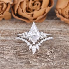 a white diamond ring sitting on top of a wooden table next to some brown roses