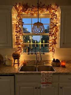 a kitchen sink under a window covered in fall leaves and lite up with fairy lights