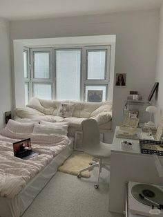 a room with a bed, desk and laptop on the floor in front of two windows