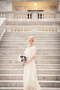 a woman in a wedding dress standing on the steps of a building holding a bouquet