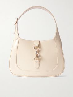 Gucci's small 'Jackie' bag takes its curved silhouette from the original style that debuted in the '60s and even boasts the same gold-tone piston clasp. Crafted in Italy from ivory patent-leather, it's suspended on a thick strap that can be adjusted to your perfect drop. It has plenty of space inside for everyday essentials, like your wallet, keys, cell and compact. White Luxury Designer Bag, Luxury Leather Miu Miu Shoulder Bag, Luxury Sleek Shoulder Baguette Bag, Luxury High-end Women's Baguette Bag, Simple Designer Bags, Hand Bag Outfit, Jackie Purse, Essentials Clothes, Latest Bags