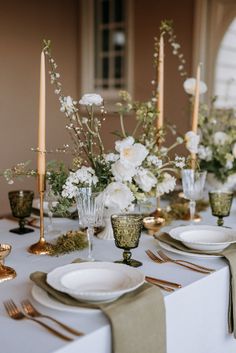 the table is set with white flowers, candles and gold place settings for an elegant dinner