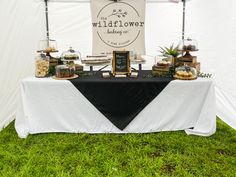 a table topped with cakes and desserts under a white tent covered in black cloth