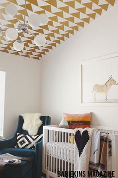 a baby's room with a white crib, blue chair and gold geometric ceiling