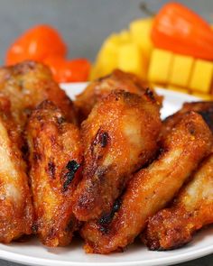 some chicken wings are on a white plate next to carrots and other food items