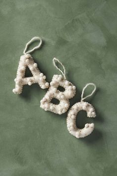 two white beaded letters are hanging from twine strings on a green cloth surface