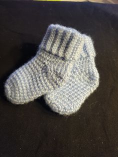 two blue knitted mittens sitting on top of a black cloth covered tablecloth