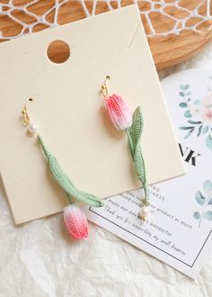 two pink and green tasselled earrings sitting on top of a piece of paper