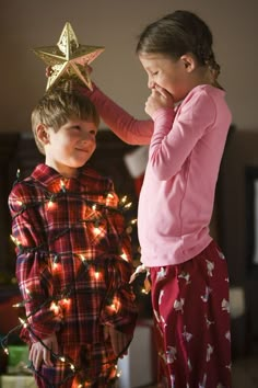 two young children standing next to each other near a christmas tree with lights on it