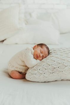 a baby wrapped in a blanket on top of a bed with white sheets and pillows