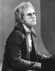 a man sitting at a piano in front of a black and white photo with glasses on