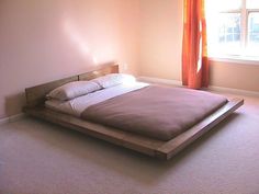 a bed sitting in the middle of a bedroom next to a window with an orange curtain