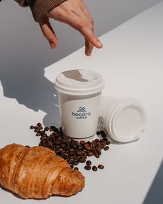 a coffee cup and croissant on a table with coffee beans next to it