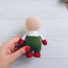 a hand holding a small crocheted doll on top of a white wooden table