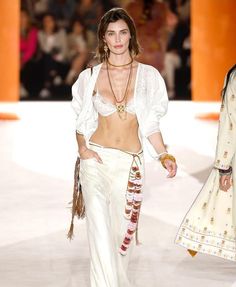 a woman walking down a runway in white clothing