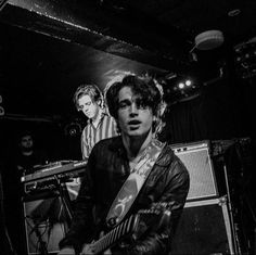 black and white photo of two young men playing guitars in front of microphones on stage