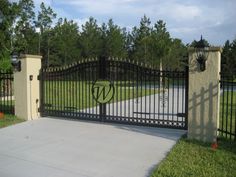 a gated driveway leading into a residential area with trees in the background and grass on either side