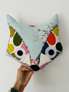 a person holding up a colorful pillow with an animal face on it's side