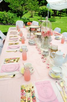 the table is set with pink and white plates, silverware, cups, and utensils