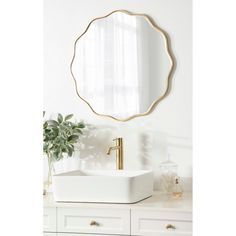 a white sink sitting under a round mirror in a bathroom next to a potted plant