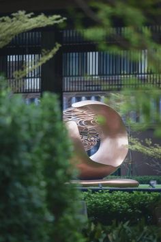 a large metal sculpture sitting in the middle of a lush green park next to a tall building