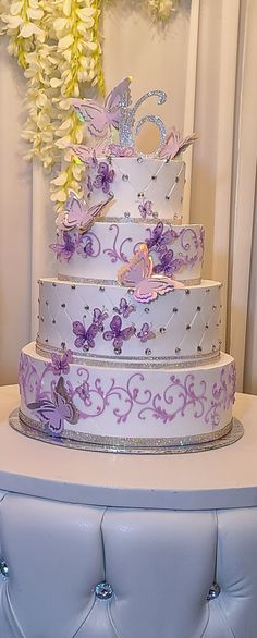 a three tiered cake with purple flowers and butterflies on the top is sitting on a blue bench