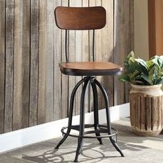 a wooden and metal bar stool next to a potted plant in front of a wood paneled wall