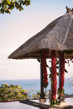 a gazebo with red flowers on it near the ocean