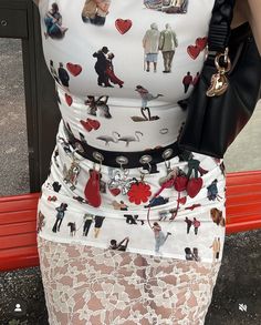 a woman is wearing a skirt with pictures on it and holding a black handbag