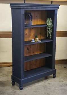 a blue bookcase with some plants on top of it and a vase in the middle