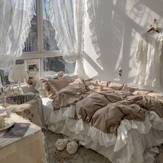 an unmade bed sitting next to a window in a room with white curtains on the windowsill