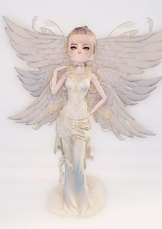 a white and gold angel figurine with wings on it's head, standing in front of a white background