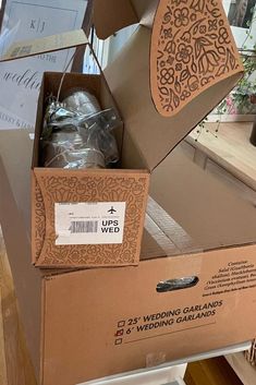 an open cardboard box on top of a table filled with flowers and other items for sale