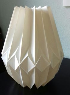 an origami vase sitting on top of a table next to a black surface