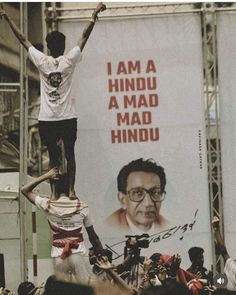 a man standing on top of another man in front of a large banner with an image of him