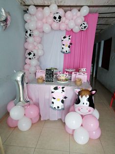 a cow themed birthday party with pink and white balloons on the wall, cake table and decorations