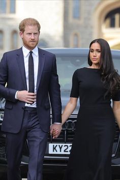 prince harry and his wife are walking hand in hand through the streets with cars behind them