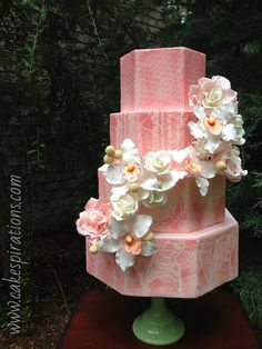 a three tiered pink cake with white flowers on top