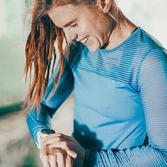 a woman with red hair is smiling and looking down at her wrist watch on her left hand