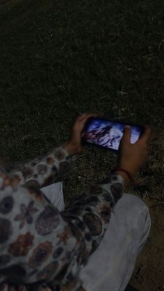 a person sitting on the ground holding up a cell phone