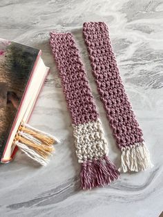 two crocheted scarfs next to an open book on a marble table top