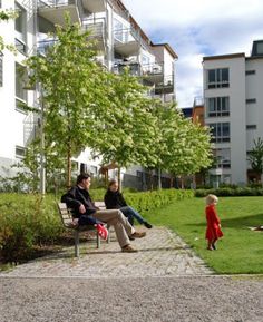 two people sitting on a bench in front of a building and a small child walking by