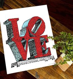 a card with the word love written in red, blue and black on it next to a potted plant