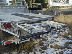 the back end of a silver truck parked on snow covered ground next to tall grass and trees