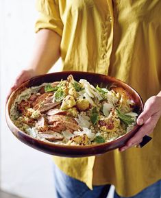 a person holding a dish with meat and vegetables on it in front of the camera