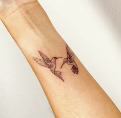 a small hummingbird tattoo on the left arm and wrist, with two birds flying around it