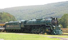 an old fashioned steam train is on the tracks in front of some trees and mountains